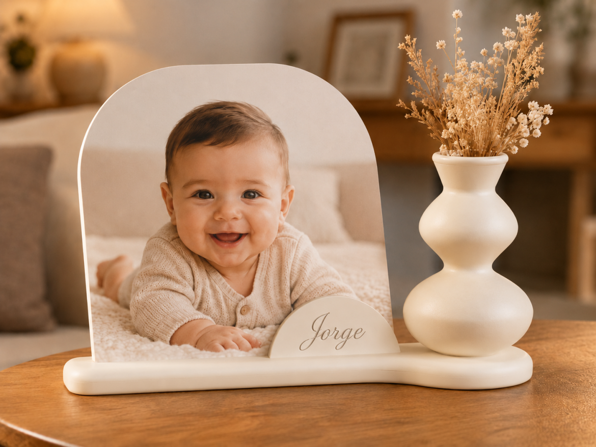 Bebé sonriente en un soporte decorativo con flores secas al lado.